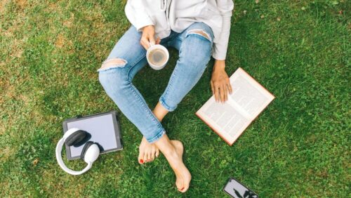 Woman sits on grass with coffee and book