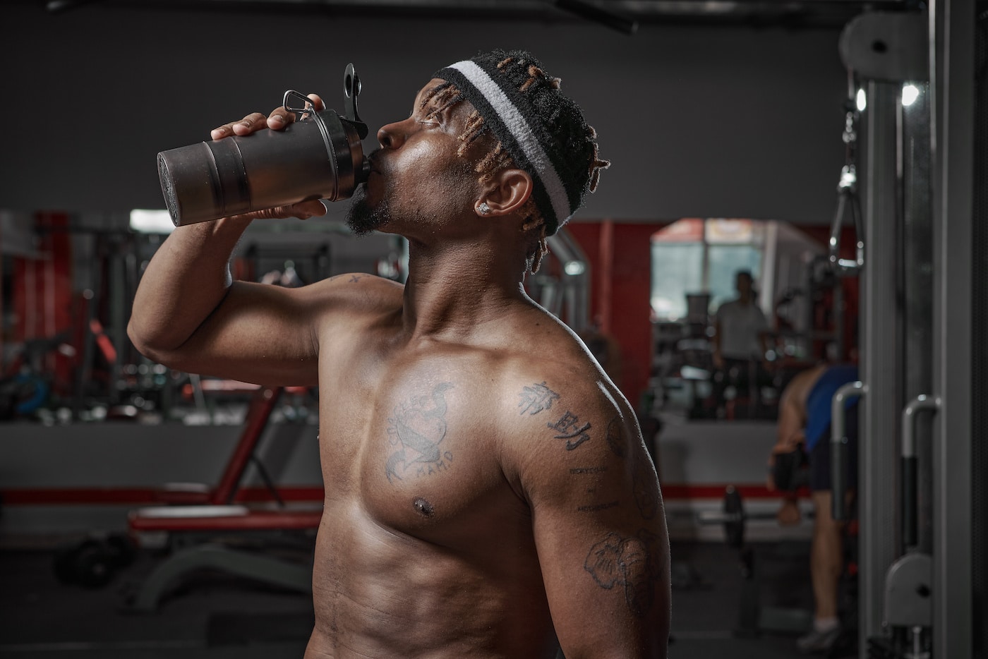 athletic man with naked torso drinking water or sports nutrition from glass after gym workout