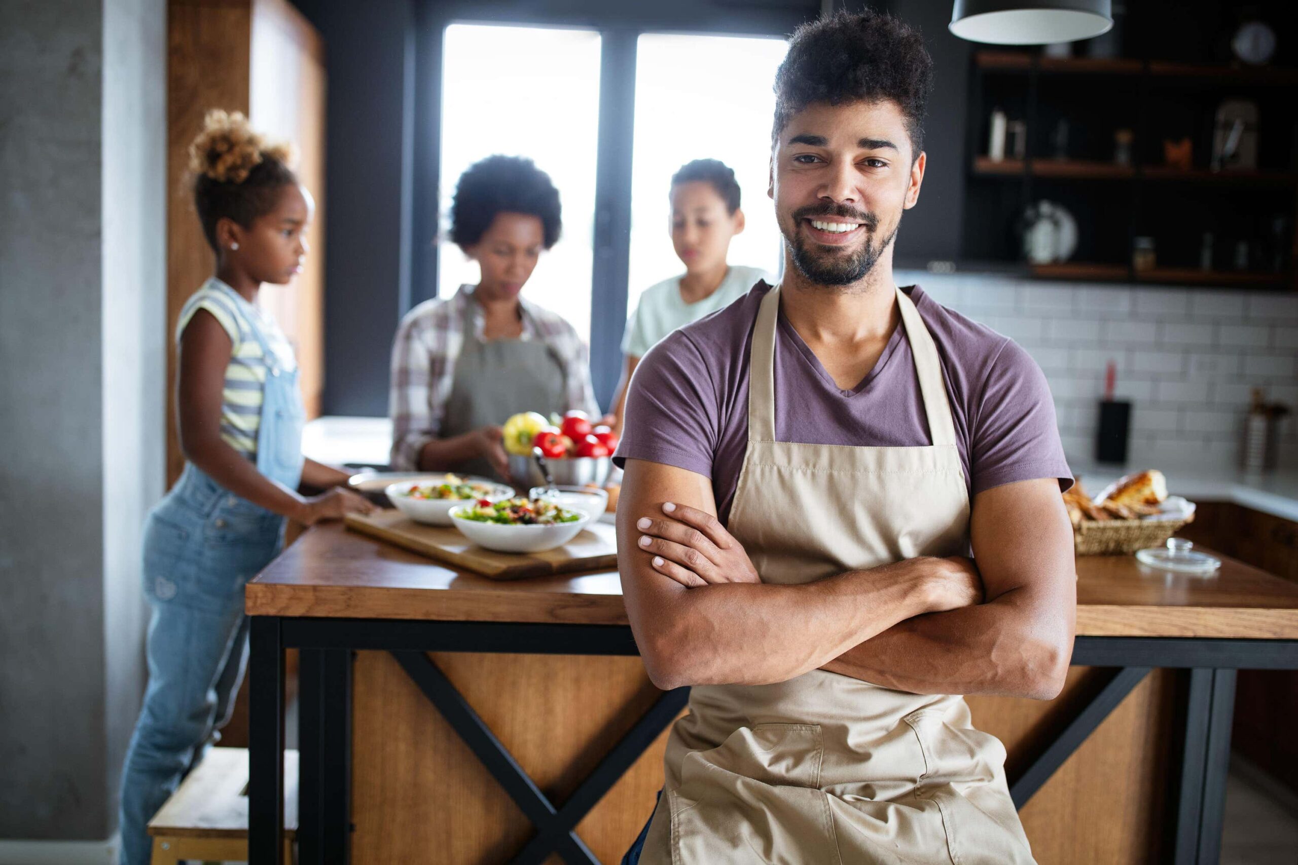young man smiles in kitchen with family behind him scaled