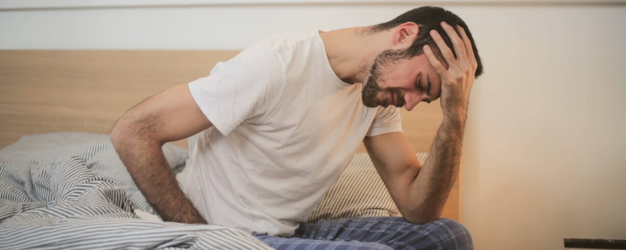 man sits on bed with hand on head
