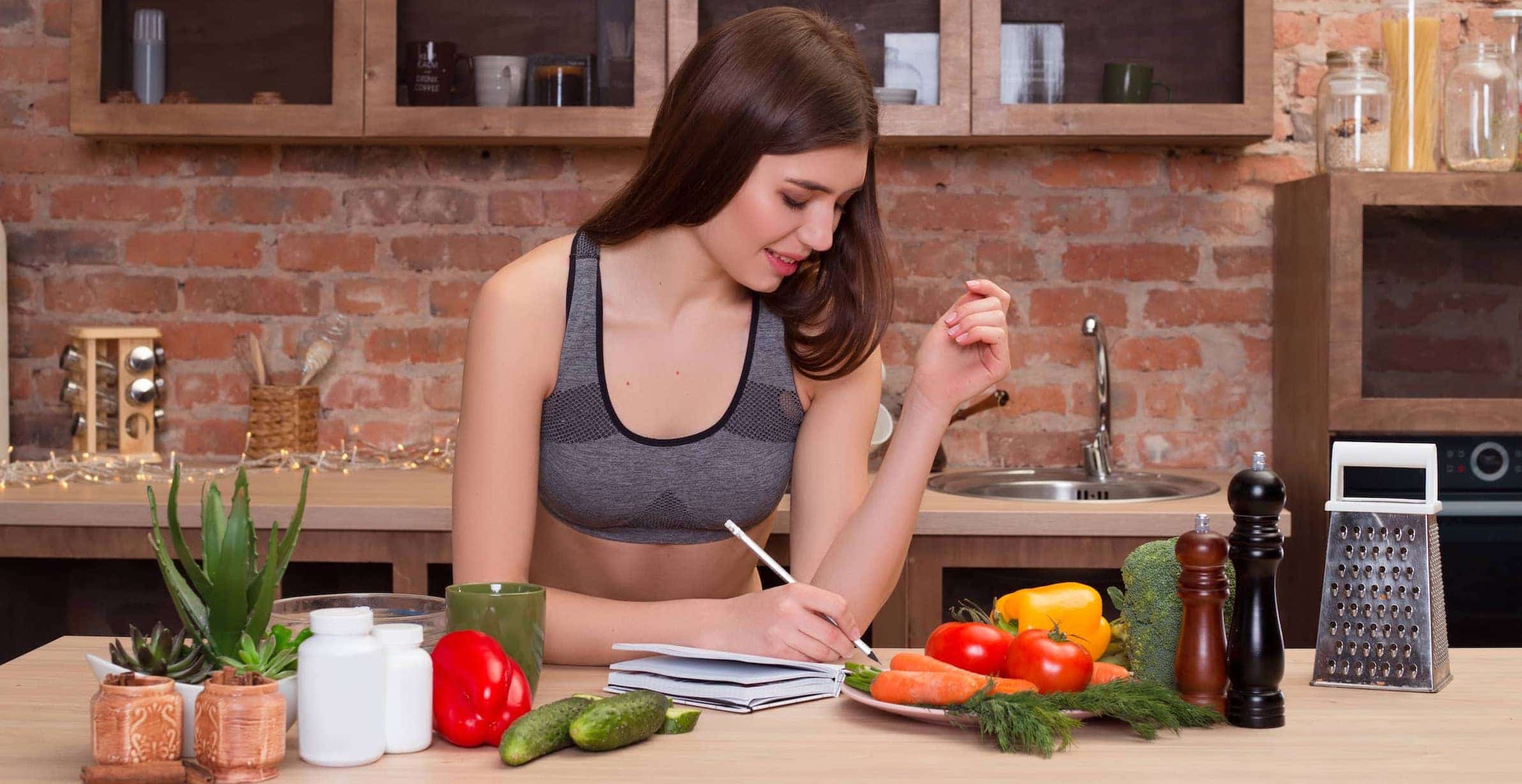 Young woman sits at the kitchen table and writes in her diary everything about healthy